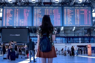 Young woman with suitcase looking at departures board at airport