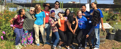 Group of 13 "Alternative breaks" program leaders making silly faces at camera, standing in front of garden of potted plants