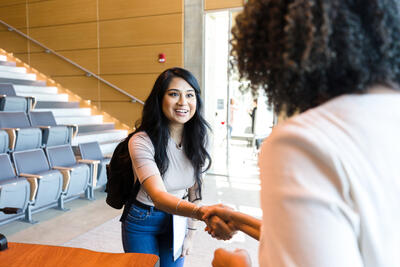 Smiling female college student smiles as she shakes hands with a female professor.