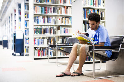 Student sitting on chair in library, looking over a book