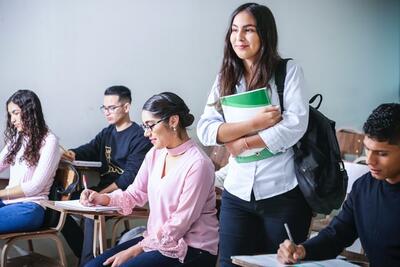 Student walking confidently through desks in classroom, holding study materials, while other students take exams 